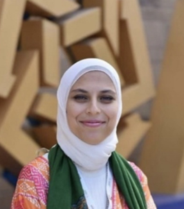 A veiled woman is smiling and standing in front of the AUC star