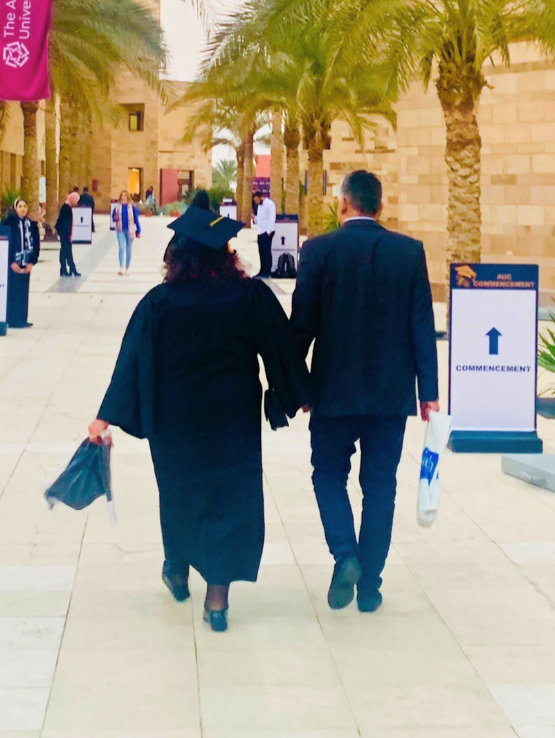 Abdel-Motaal walks hand-in-hand with her son on campus to commencement, wearing her cap and gown 