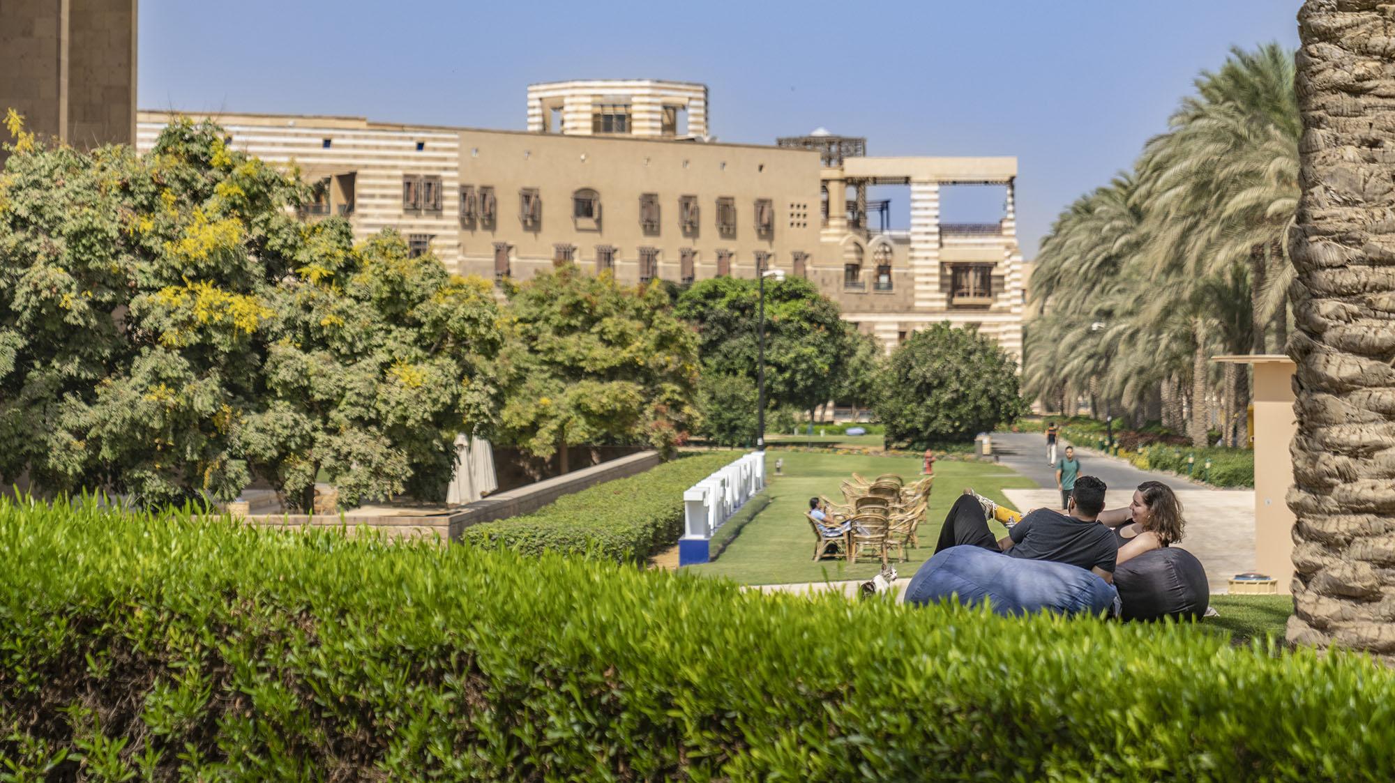 Students sitting in a garden with a beige building in the back