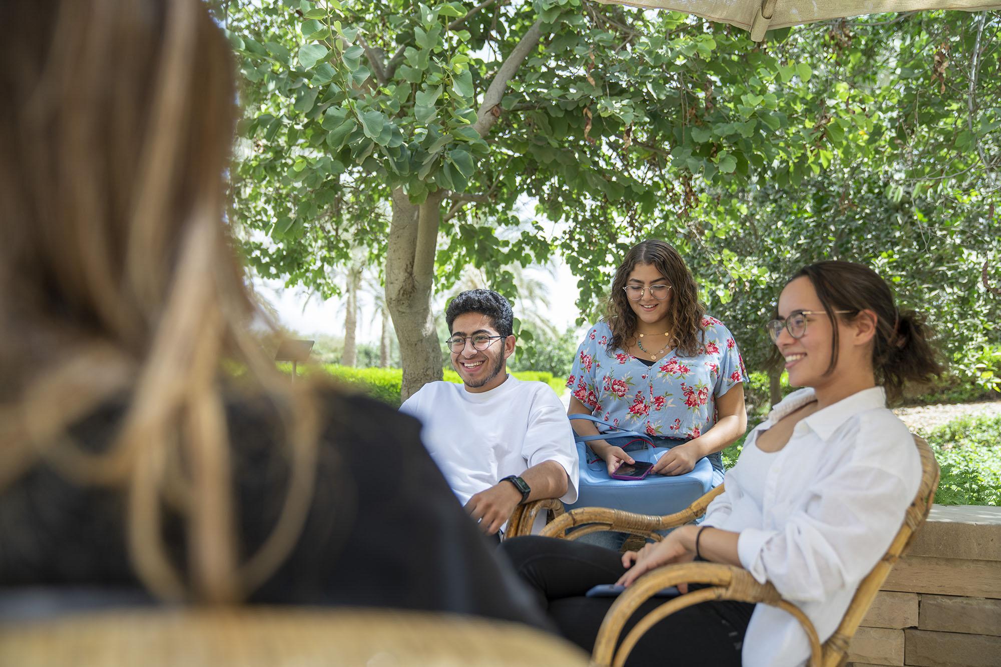 Two girls and a boy sitting outside in a garden smiling and talking