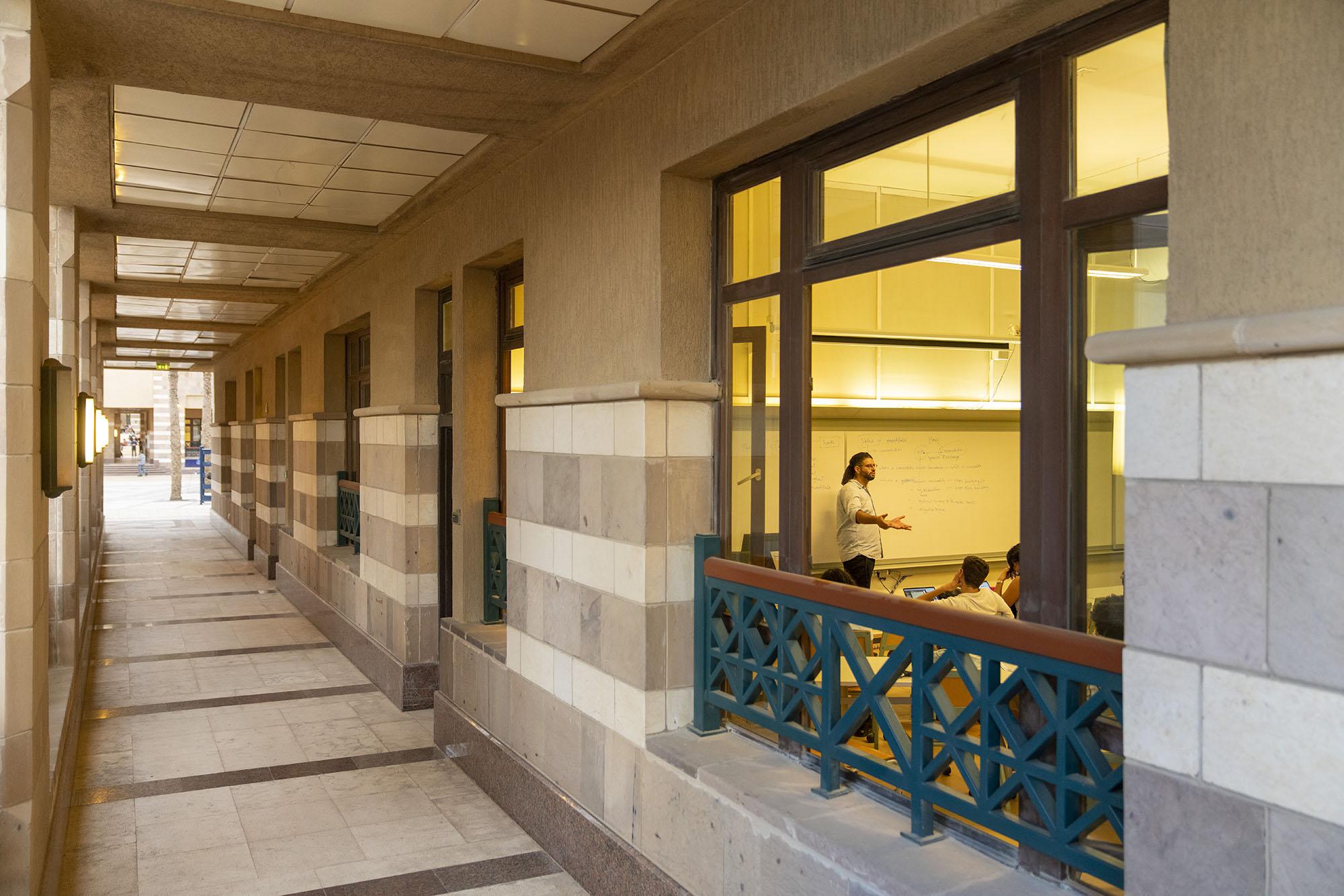 Instructor standing and talking to students in class. View is from the outside of the classroom.