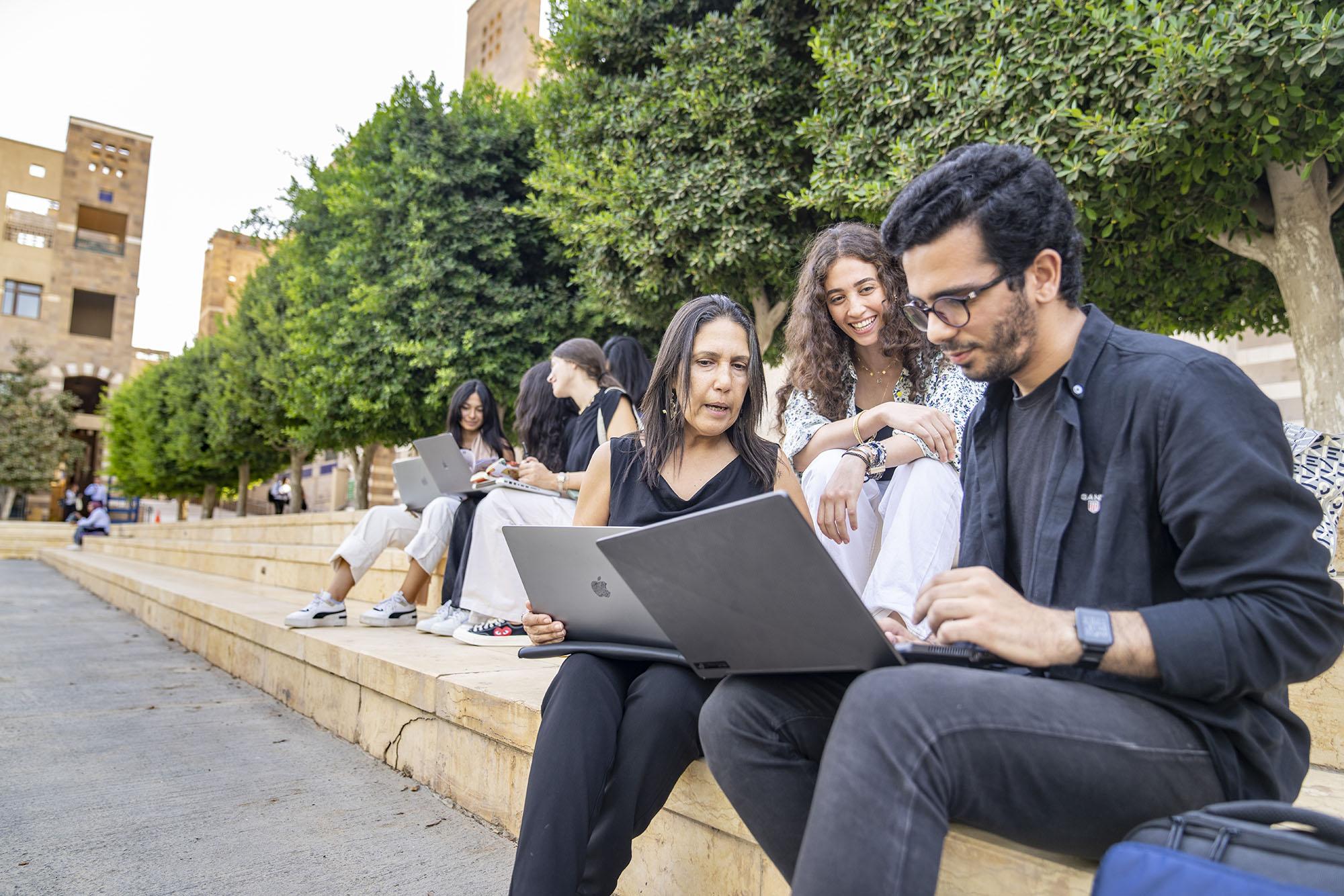 Nagla Samir explaining information on laptop with male and female students in campus garden