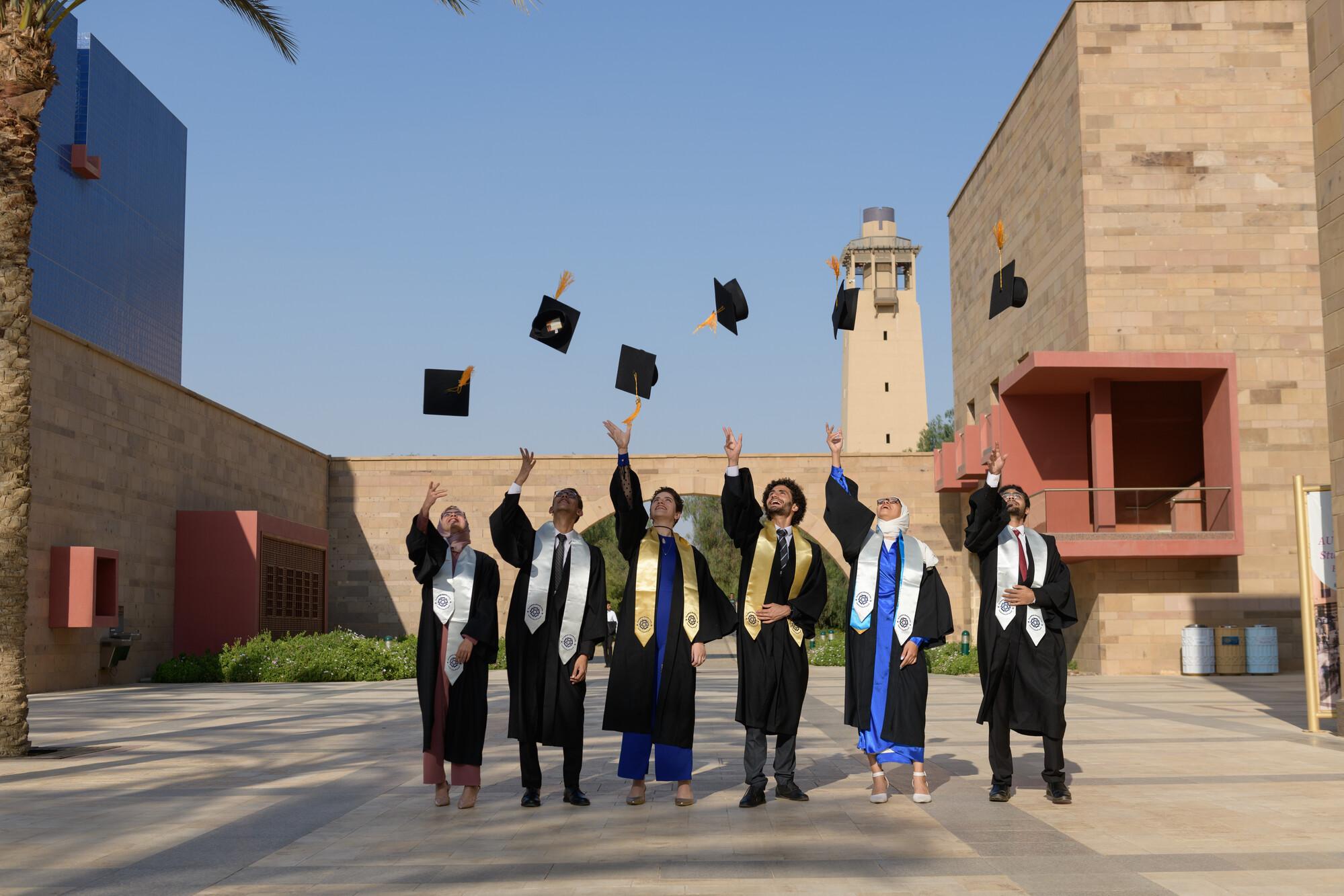 A group of students wearing gowns and throwing their cap in the air on AUC campus