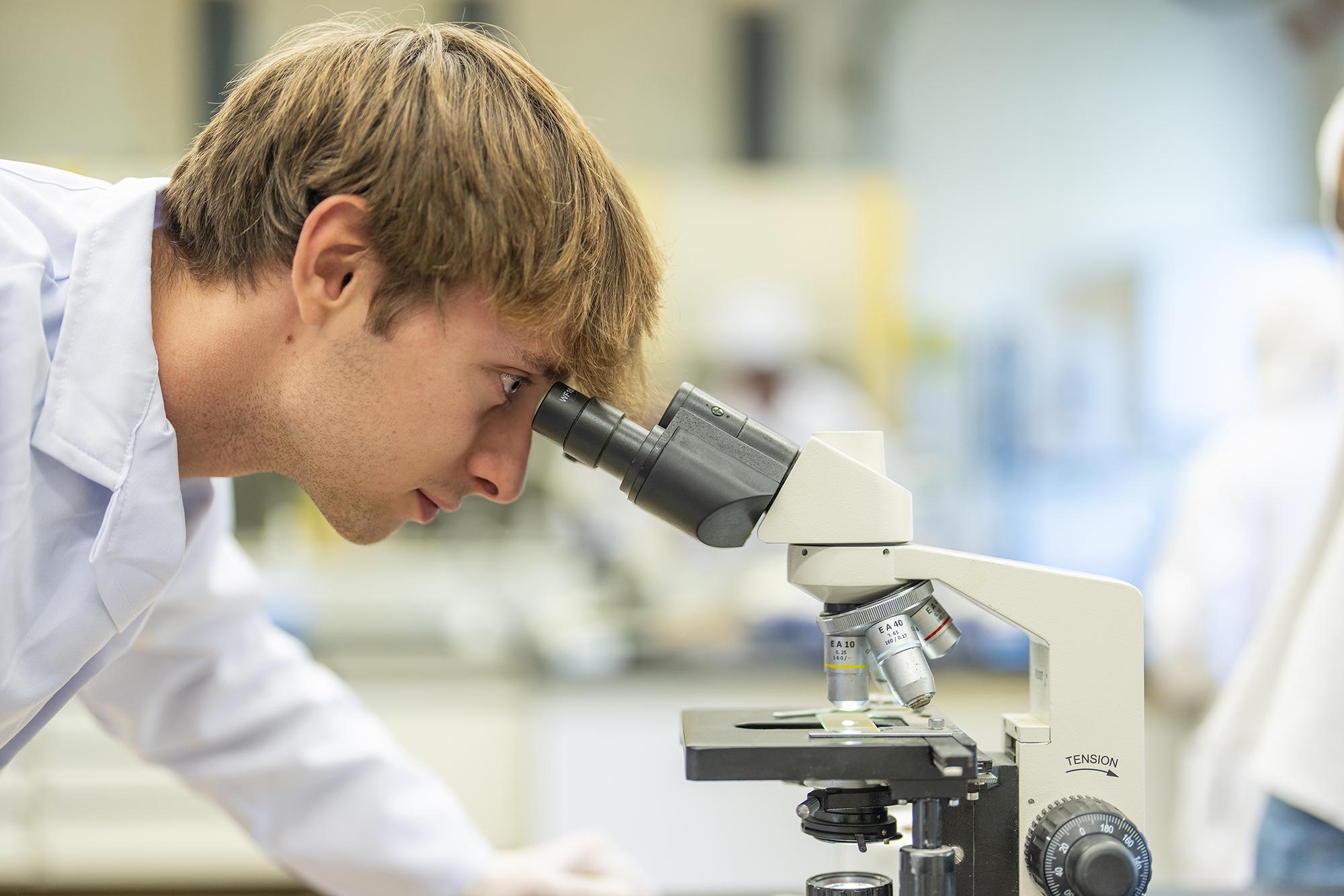 A blond boy in a research lab looking through a microscope