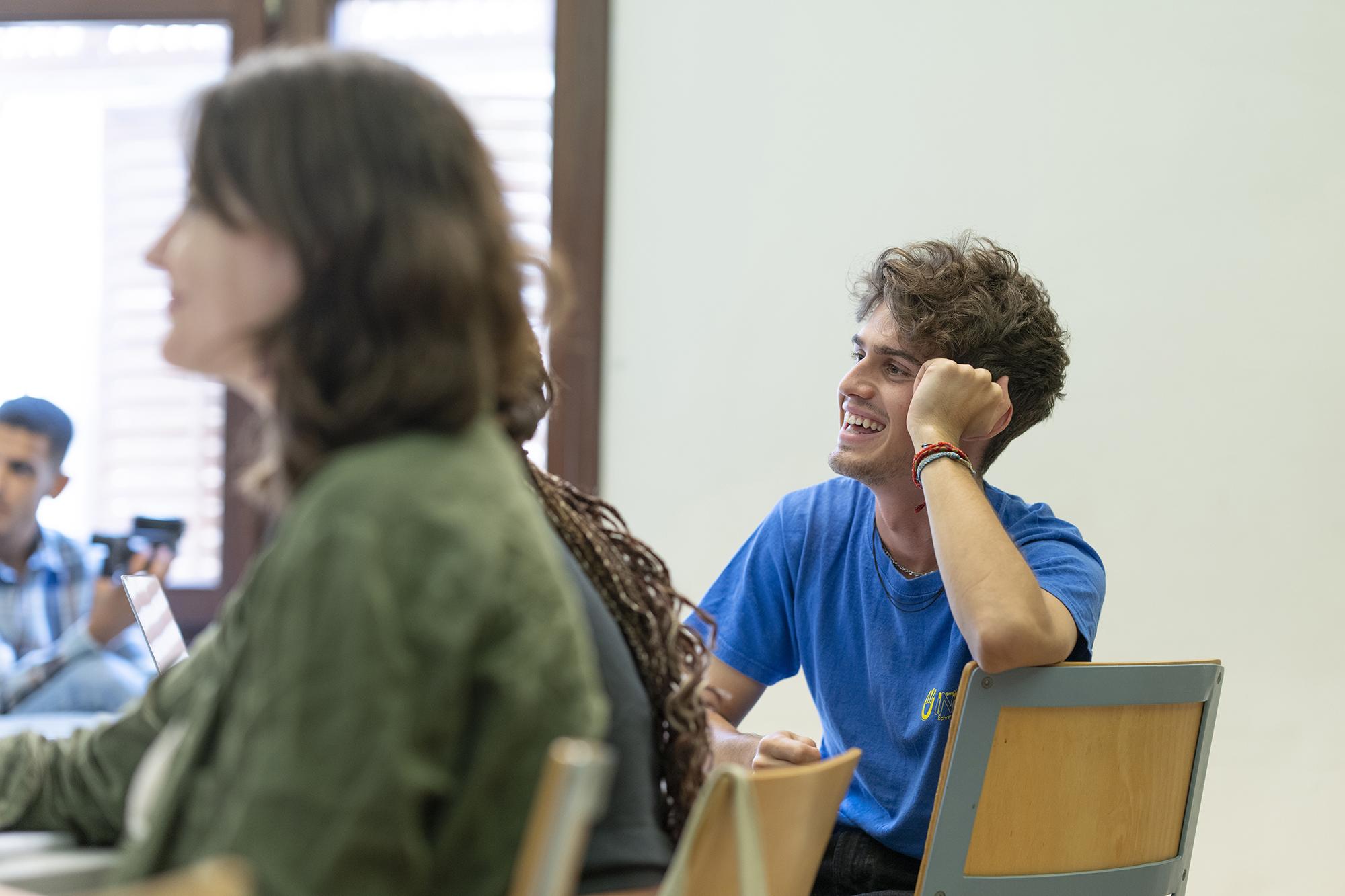 A student wearing a blue tshirt sitting in a classroom and smiling
