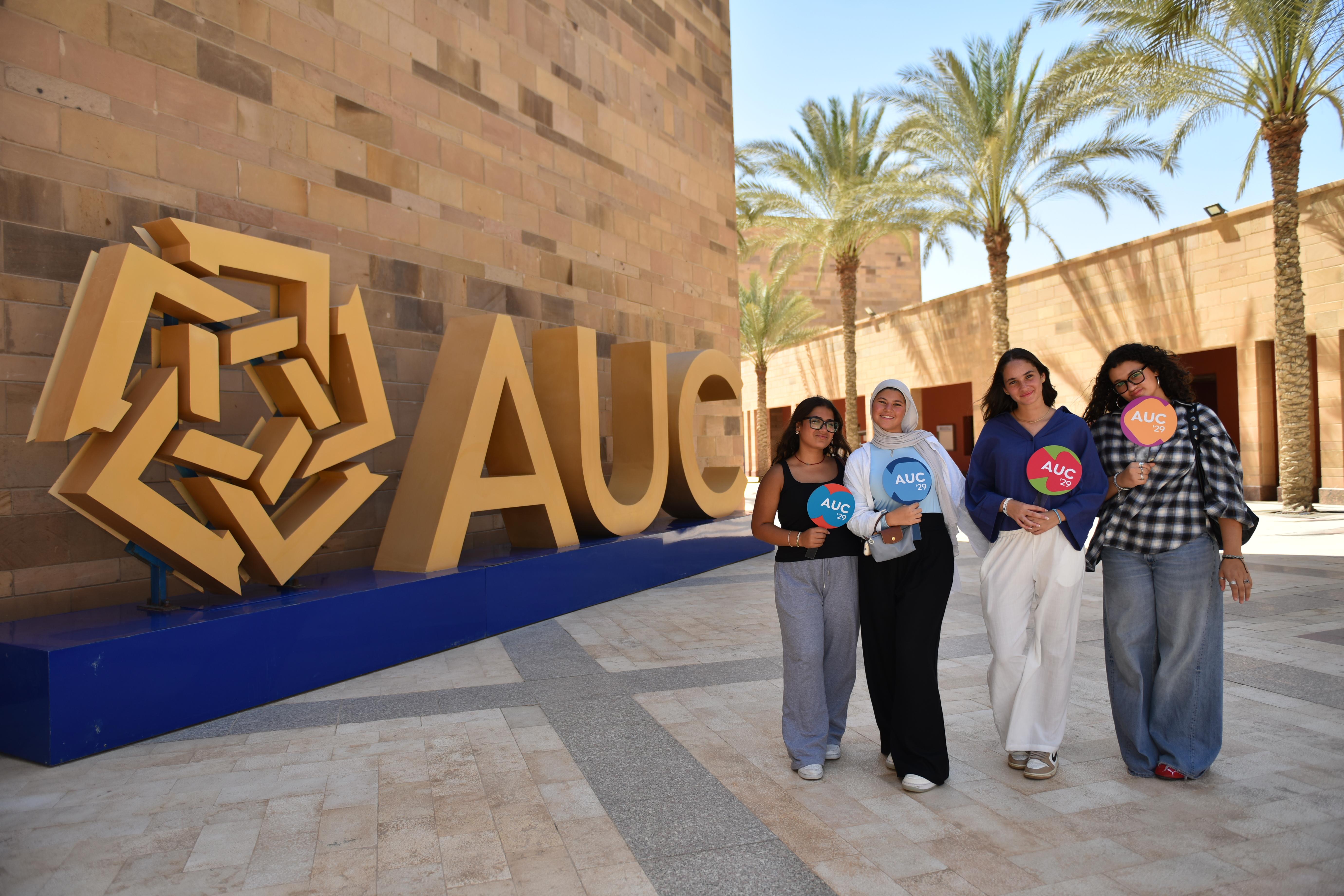 four female students walking on campus holding a round sign with AUC '29 on it