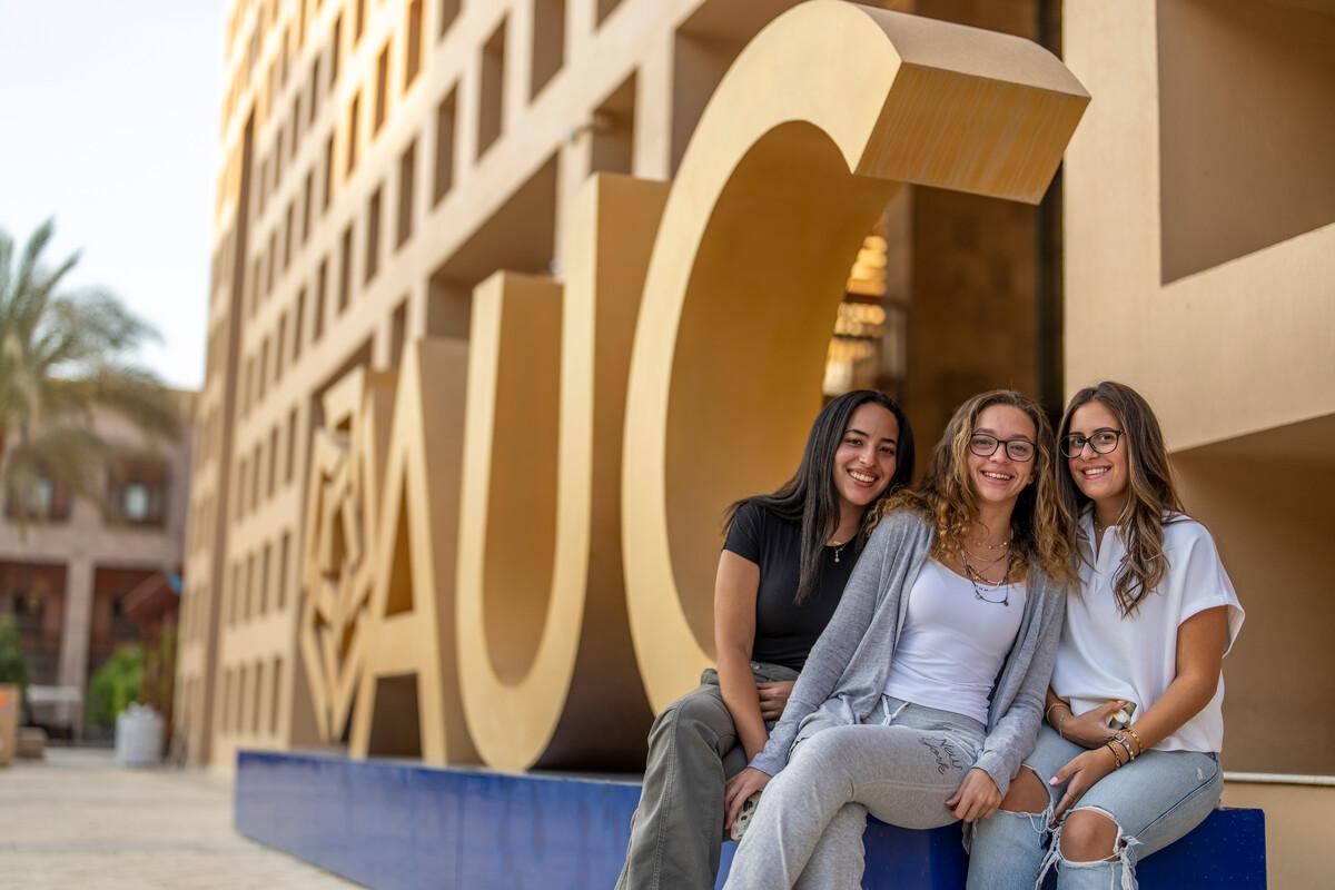 students sitting next to AUC logo in the Bartlett Plaza