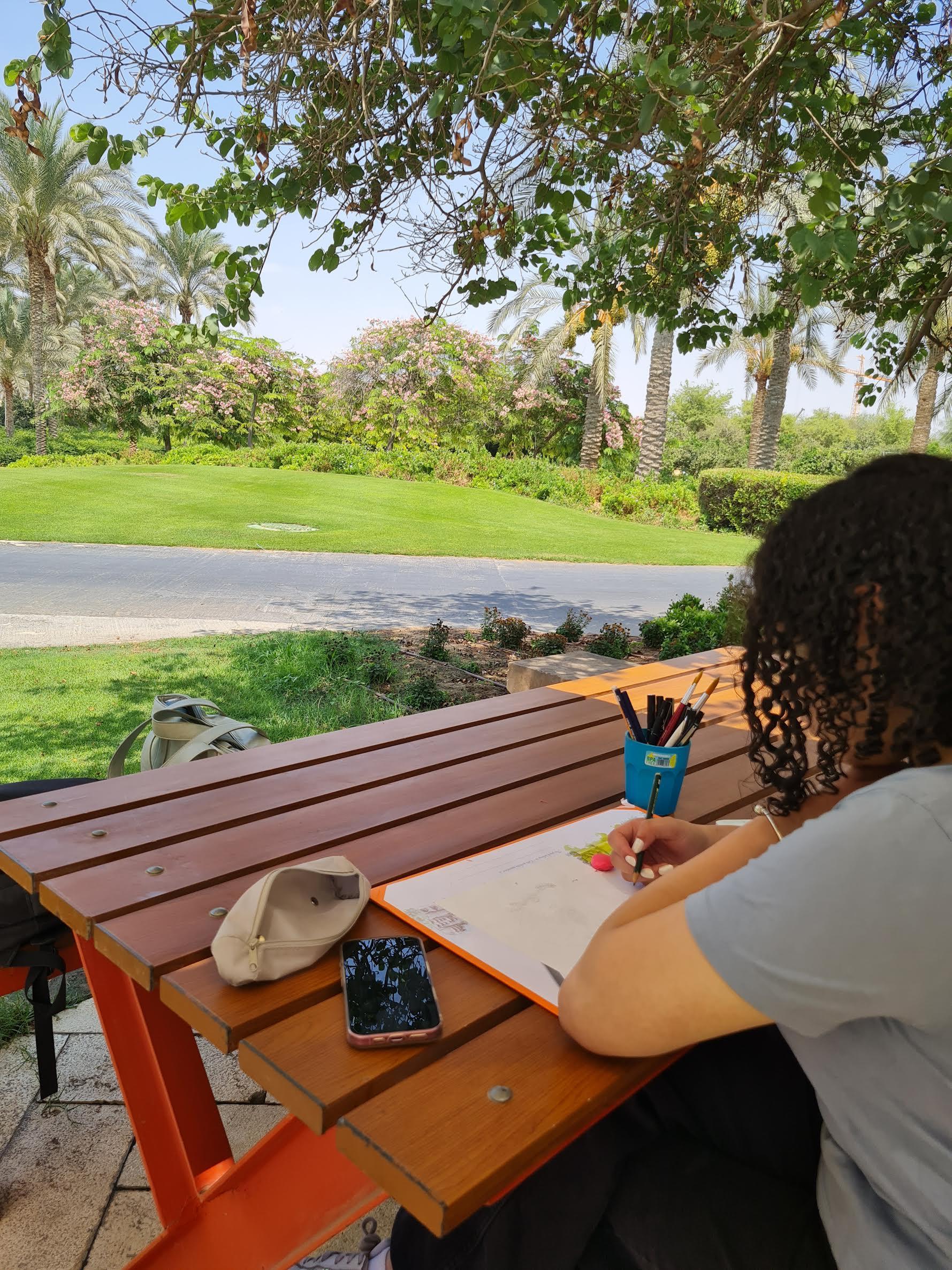 a girl with curly black hair sitting on the benches and drawing on a piece of paper