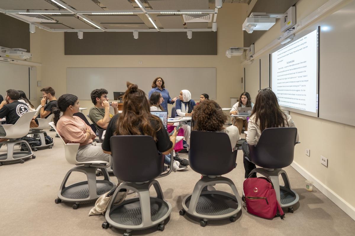 Students participate in a discussion-based class in a modern AUC smart classroom with projected materials.