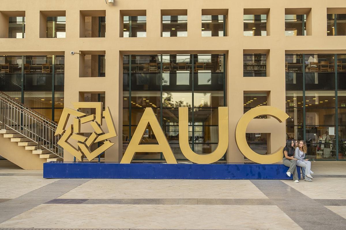 Students sitting next to the AUC big letters in front of a building