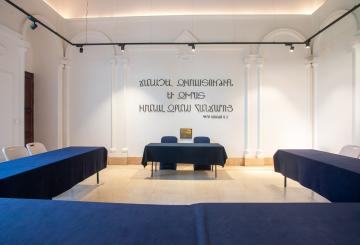 Chairs and tables in a room with Armenian text on the wall that reads To acquire wisdom and guidance, learn the knowledge of the intellect.