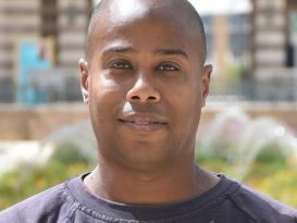 Headshot of a man in an outdoor setting wearing a black tshirt