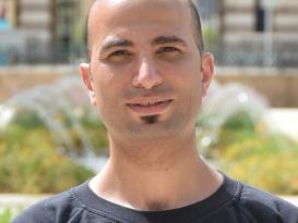 Headshot of a smiling man in an outdoor setting wearing a black tshirt