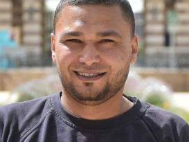 A headshot of a man smiling wearing a black tshirt in an outdoor setting