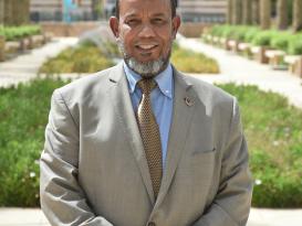 A man smiling wearing a suit and tie in an outdoor setting