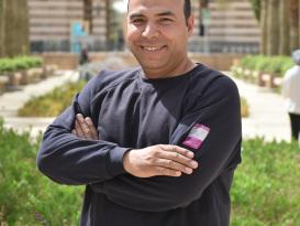 Headshot of a man smiling with crossed hands in an outdoor setting