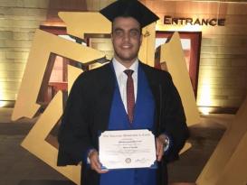 A boy wearing cap and gown holding his certificate