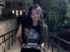 A female is standing, smiling and holding a trophy that has the letters A U C and an eagle next to the letters