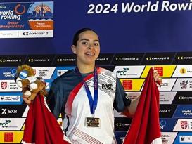 A female is smiling and holding the Egyptian flag and a plush toy, she is wearing a medal. Text behind her: 2024 World Rowing