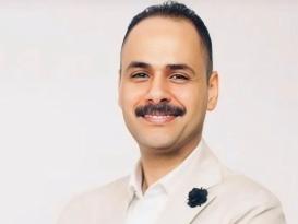 A man with a moustache is smiling and crossing his arms