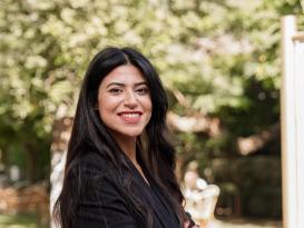 a girl with long black hair wearing all black and crossing her hand smiling
