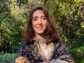 Anastasia stands in a shawl with her arms crossed, outdoors