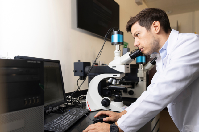 A scientist in a lab coat peers through a microscope.