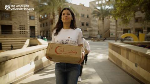 A female students carrying a cardboard box on campus