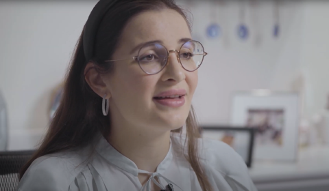 A woman is wearing glasses and she is sitting indoors