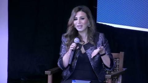 A woman is sitting on a chair and speaking into a microphone