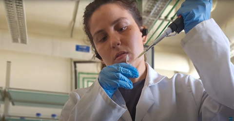 A girl in a lab wearing a lab coat and holding a plastic applicator