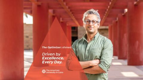 A male wearing glasses is standing next to red pillars. Text reads "The Facilitator: Ahmed. Driven by Excellence. Every Day. The American University in Cairo"
