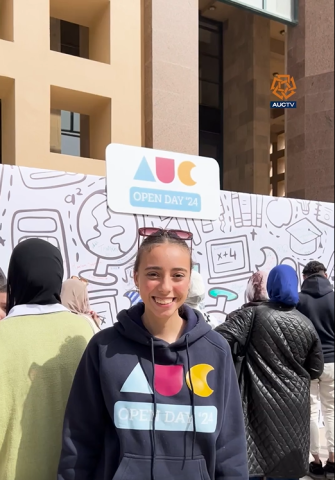 A female is smiling and wearing a hoodie that reads "AUC Open Day '24"