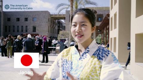 A Japanese girl wearing a kimono and smiling. People are standing in the background. The Japanese flag is displayed. Text reads "The American University in Cairo"