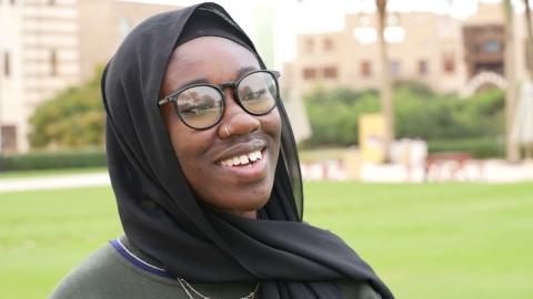 A girl is smiling. She is veiled and wearing glasses