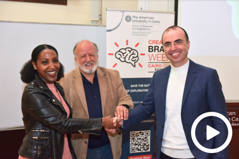 Two men and a woman shake hands in front of a banner from Brain Week 2024