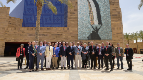 Many people in business casual wear pose in front of a tall beige building