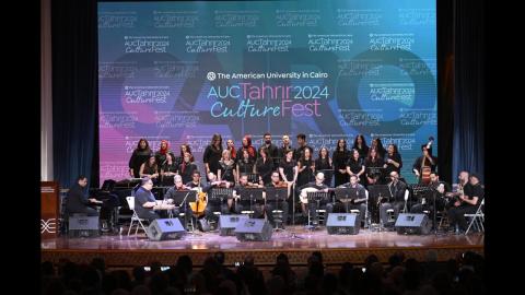 Musicians playing instruments and men and women singing on stage in fron of a backdrop withg the text "The American University in Cairo. AUC Tahrir CultureFest 2024"