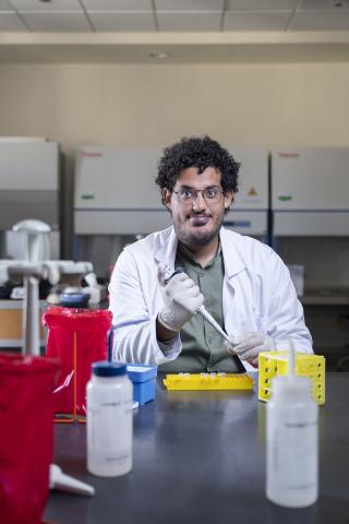 A male student is wearing a white coat in a lab