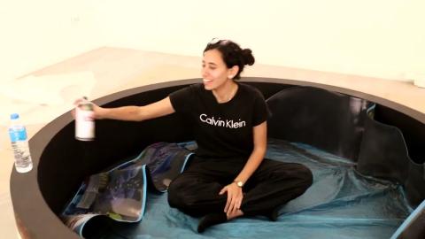 A female is sitting in a circle and holding a can of spray. There is a bottle of water on the edge of the circle. Text on T-shirt: Calvin Klein