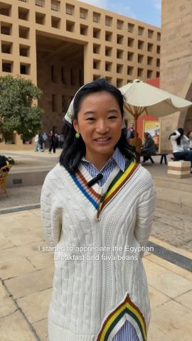 A female is standing with her hands behind her back and she is smiling