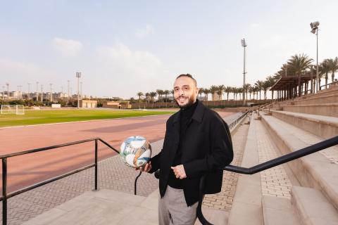 A man is standing in a field, he is smiliong and holding a football in his hand