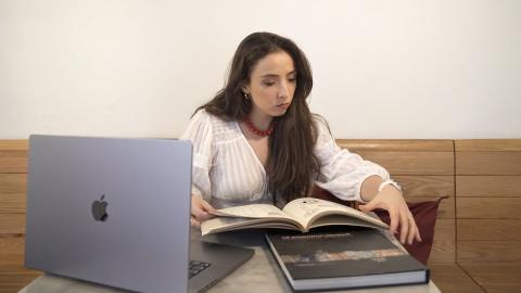 A female is looking at books and there is a laptop in front of her