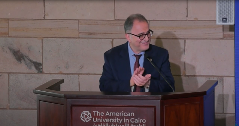 A man is standing at a podium and clapping. Text: The American University in Cairo