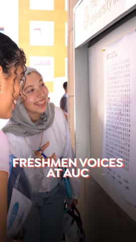 Two females are standing in front of a word finding puzzle. Text: Freshman Voices at AUC