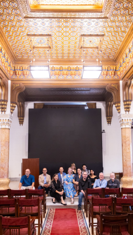 Multinational males and females are sitting in an old, decorated hall and smiling