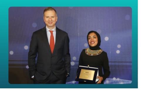 A man and a woman are standing and smiling, and she is holding an award