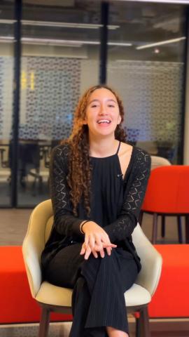 a girl with orange hair wearing all back sitting on a chair and posing at the camera