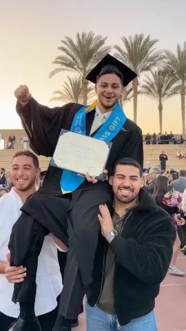Two males are carrying a male on their shoulder. They are wearing caps and gowns and smiling