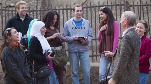 Males and females are standing and laughing next to an old iron fence in tye street